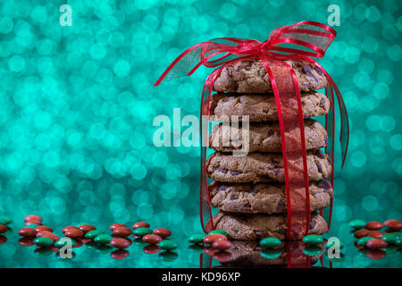 Pile de cookies aux pépites de chocolat avec des bonbons rouges et verts la réflexion sur la table en verre sur fond vert Banque D'Images