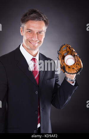 Mature businessman holding baseball et mitt sur fond noir Banque D'Images