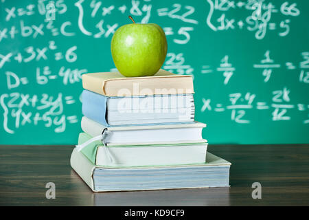 Pile de manuels scolaires et apple in front of blackboard Banque D'Images