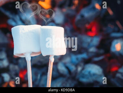 Deux guimauves grillées sur sweet white fire flames. fumer sous forme de coeur. de la guimauve en brochettes rôti sur fusains Banque D'Images