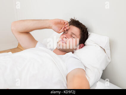 Jeune homme souffrant de maux de tête Lying On Bed Banque D'Images