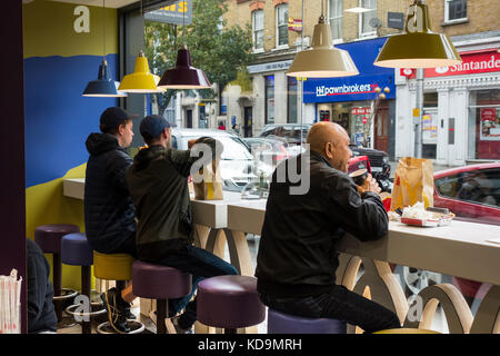 Trois hommes mangent dans un restaurant McDonald's de Acton High Street, Londres, Angleterre, Royaume-Uni Banque D'Images