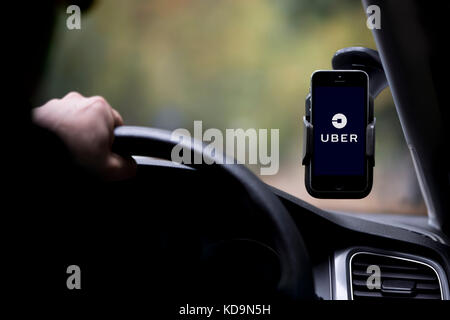 Portrait d'un homme dont le visage est caché derrière un taxi Uber, disques durs et a le logo de l'entreprise sur son smartphone qui est fixé sur le pare-brise. Banque D'Images