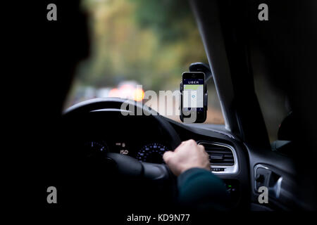 Portrait d'un homme dont le visage est caché derrière un taxi Uber, disques durs et a le logo de l'entreprise sur son smartphone qui est fixé sur le pare-brise. Banque D'Images