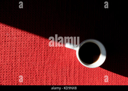 Une tasse de café est sur une table rouge, à demi couvert dans le soleil et la moitié à l'ombre Banque D'Images