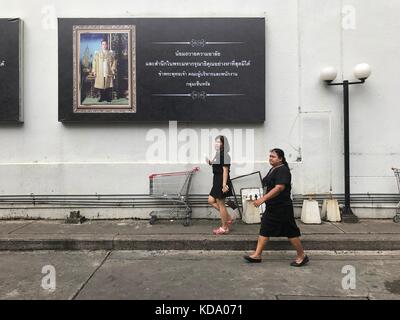 Bangkok, Thaïlande. 11 octobre 2017. Deux thaïlandais habillés de noir marchant devant une affiche représentant le défunt roi Bhumibol de Thaïlande à Bangkok, Thaïlande, le 11 octobre 2017. Le roi meurt le 13 octobre 2016. Des invités officiels du monde entier sont attendus pour la crémation le 26 octobre 2017. Crédit : Christoph Sator/dpa/Alamy Live News Banque D'Images