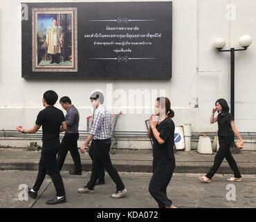 Bangkok, Thaïlande. 11 octobre 2017. Des thaïlandais vêtus de noir marchant devant une affiche représentant le défunt roi Bhumibol de Thaïlande à Bangkok, Thaïlande, le 11 octobre 2017. Le roi meurt le 13 octobre 2016. Des invités officiels du monde entier sont attendus pour la crémation le 26 octobre 2017. Crédit : Christoph Sator/dpa/Alamy Live News Banque D'Images