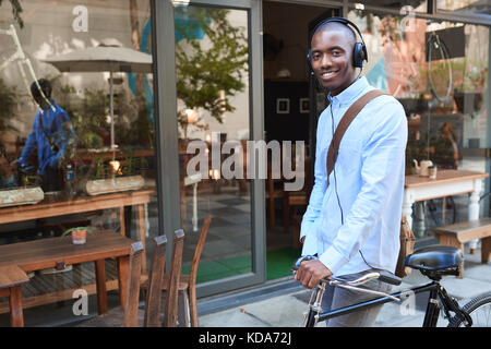 Smiling young man standing avec son vélo portant des écouteurs Banque D'Images