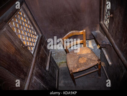 Église catholique confessionnelle cadre confessionnel rustique vue intérieure du petit fauteuil en osier du prêtre dans un simple confessionnel en bois dans une église catholique romaine Banque D'Images