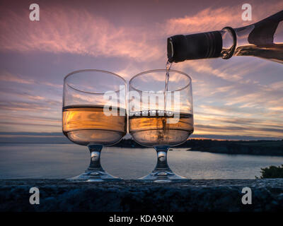 Verser le vin de Rosé sur un banc de pierre avec coucher de soleil et mer derrière dans un cadre romantique et paisible KERFANY LES PINS BRETAGNE Banque D'Images