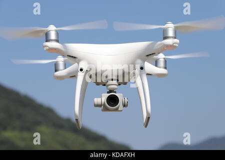 Drone télécommandé blanc volant dans ciel bleu clair avec vue sur la montagne Banque D'Images