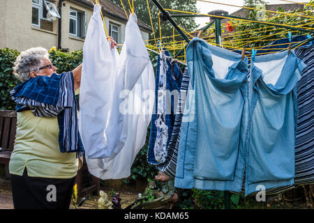 Un vieux / personnes âgées / senior lady (80 ans) sortir blanchissage dans son jardin, par une chaude journée, au début de l'automne. Au sud ouest de Londres, Ealing W5, Angleterre, Royaume-Uni. Banque D'Images