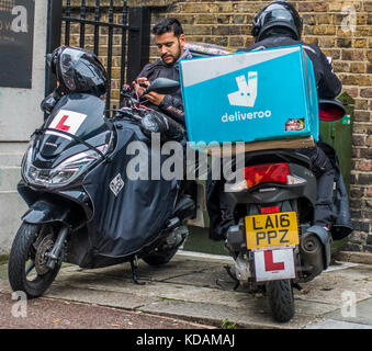 Deux hommes (deliveroo société de livraison de nourriture en ligne), les motards en prenant une pause dans l'exécution des commandes à Londres, Angleterre, Royaume-Uni. Banque D'Images