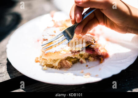Les enfants manger du fromage et d'un strudel aux cerises avec du sucre sur le dessus de la main de l'enfant. avec la fourchette est de manger de délicieuses pâtisseries est servi et mangé sur une plaque sur woode Banque D'Images