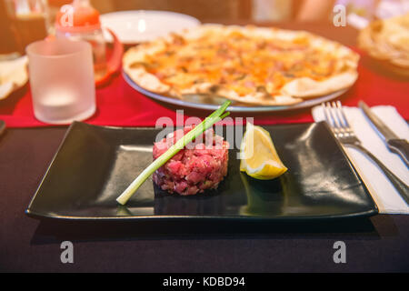 Partie de leur tartare de boeuf avec des quartiers de citron sur la plaque noire sur la table à café. La structure horizontale. Banque D'Images