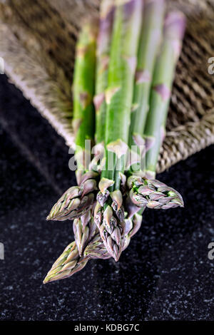 Une bande d'asperges fraîches dans un panier sur un fond sombre Banque D'Images