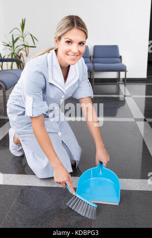 Happy maid balayant le sol avec duster et compartiment à poussière Banque D'Images