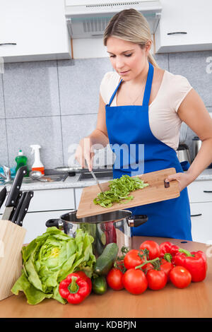 Jeune femme de mettre les légumes dans le même ustensile Banque D'Images