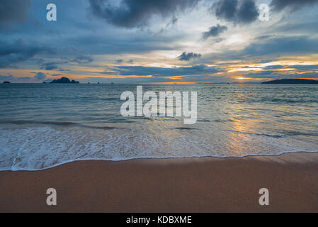 Belle plage de sable et des vagues, à l'horizon le soleil se couche sur les montagnes Banque D'Images