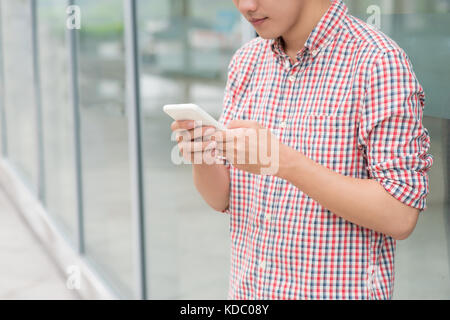 Happy asian man smiling pendant qu'il lit un message texte à l'extérieur du bureau permanent Banque D'Images