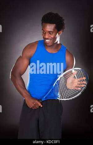 Joyeux jeune Africain tenant une raquette de tennis sur fond noir Banque D'Images
