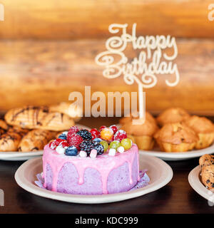 Gâteau d'anniversaire et des muffins avec un signe de vœux sur fond rustique en bois. chanter avec lettres joyeux anniversaire et maison de bonbons. Banque D'Images