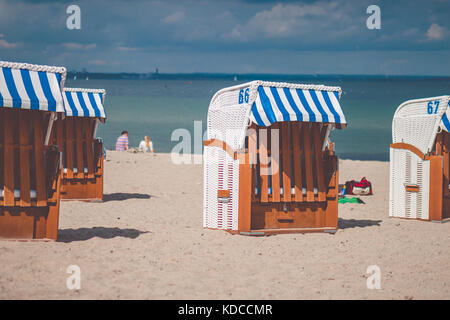 Colorfuled bar d'chaises couverte sur sable à Travemunde. Un couple sitting on beach en arrière-plan. Lübeck, Allemagne Banque D'Images