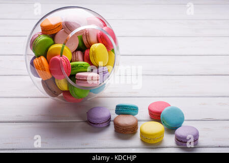 Différents types de macarons dans motion relevant de vase transparent sur un fond de bois blanc Banque D'Images