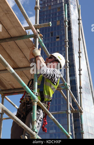 Un scaffolder érige une plate-forme de travail temporaire sur une tour au-dessus de Londres. Affiche du harnais de sécurité en usage. Le fragment est dans l'arrière-plan. Banque D'Images