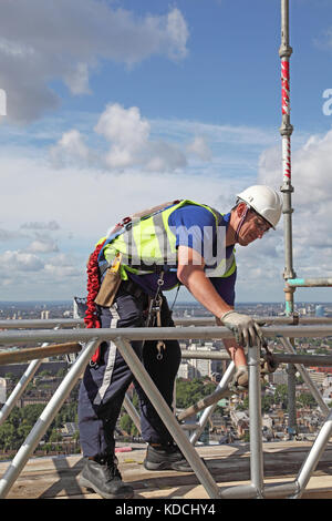 Un scaffolder érige une plate-forme de travail temporaire sur une tour au-dessus de Londres. Affiche du harnais de sécurité en usage. Banque D'Images