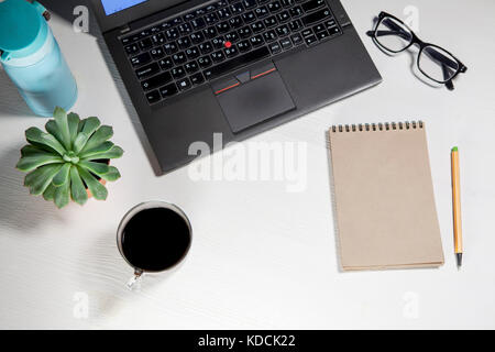 Vue de dessus de bureau blanc bureau avec ordinateur portable Clavier, plant, tasse de café, des verres et d'articles de papeterie la maquette. Banque D'Images