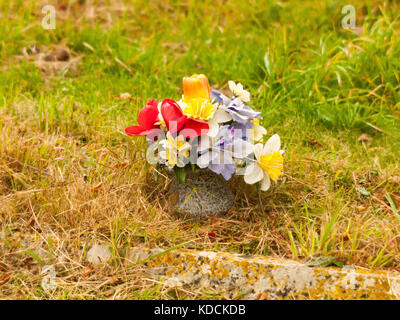 Bouquet de fausses fleurs en plastique sur l'herbe ; grave ; Essex, Angleterre, Royaume-Uni Banque D'Images