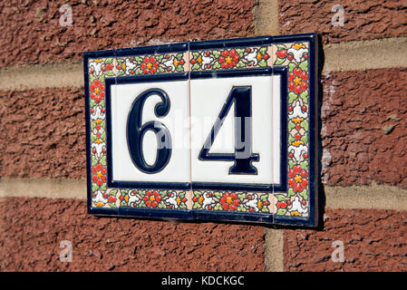 Le nombre soixante-quatre construits à partir de carreaux de céramique décoratifs, attaché à un mur de brique rouge. signifiant l'adresse d'une maison. Banque D'Images