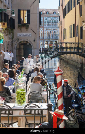 Les touristes appréciant les soleil du printemps au bord du canal de l'alimentation au Ristorante da Raffaele, San Marco, Venise, Italie avec les gondoles et gondoliers Banque D'Images