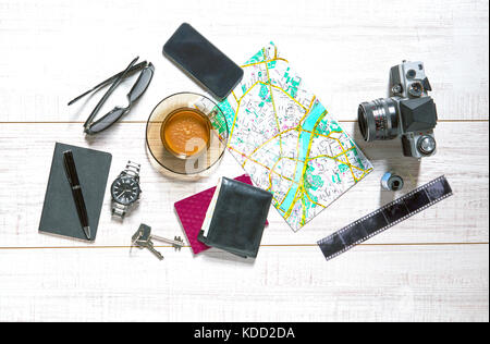 Vue d'une table en bois avec une carte, montre, passeport, ordinateur portable, smartphone, clés, ancien appareil photo, film, stylo, portefeuille, lunettes de soleil et une tasse de café dessus Banque D'Images