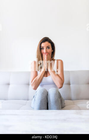 Une belle jeune femme regardant anxieusement quelque chose sur un écran toute seule à la maison. Banque D'Images