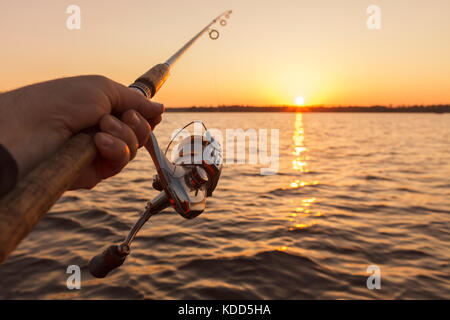 La canne à pêche dans la main sur fond coucher de soleil.solar chemin. Banque D'Images