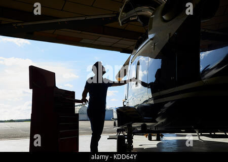 Silhouette d'homme aero ingénieur travaillant sur helicopter in hangar Banque D'Images