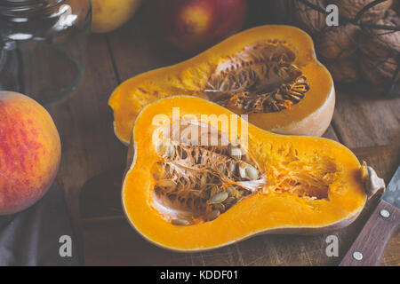 Réduit de moitié venu de courge Butternut pumpkin sur planche à découper en bois. les pêches, les nectarines, les noix, les ingrédients du smoothie sur table de cuisine rustique, tonique, t Banque D'Images