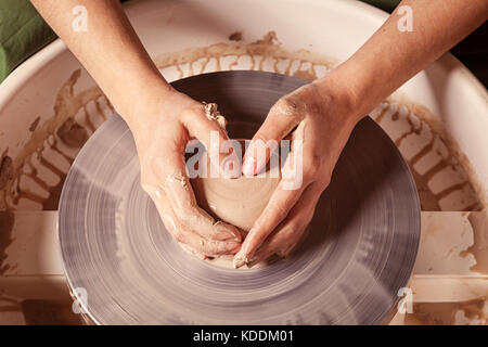 Close-up une femelle potter tenant la main sous la forme d'un coeur et magnifiquement sculpte à partir d'une argile brune une tasse profonde sur un tour de potier, une vue de dessus Banque D'Images