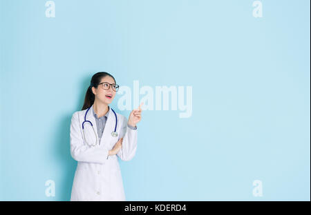 Heureux succès étudiant laboratoire femelle doctor looking at medical zone vide et faire de geste de pointage montrant idée isolé sur fond mur bleu. Banque D'Images