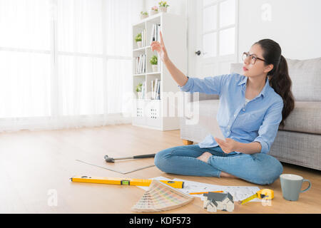 Belle femme designer sérieusement dans la salle de séjour plancher en bois et papier croquis holding avec contrôle de la main house interior design à la maison. Banque D'Images