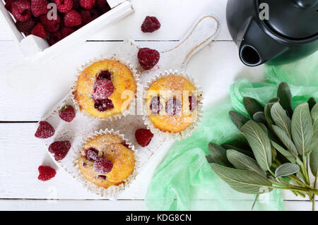 De délicieux muffins aux framboises fraîchement cuits, décoré avec du sucre en poudre, une théière sur fond de bois blanc. vue d'en haut. Banque D'Images