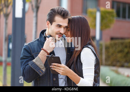 Jeune couple branché avec un casque à l'écoute de la musique ensemble au parc, automne, l'amour Banque D'Images