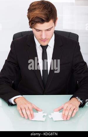 Portrait of a young businessman solving puzzle in office Banque D'Images