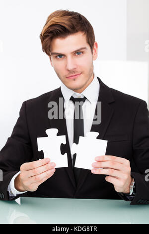 Portrait of a young businessman solving puzzle in office Banque D'Images