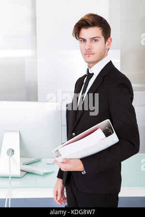 Handsome young businessman holding folder in office Banque D'Images