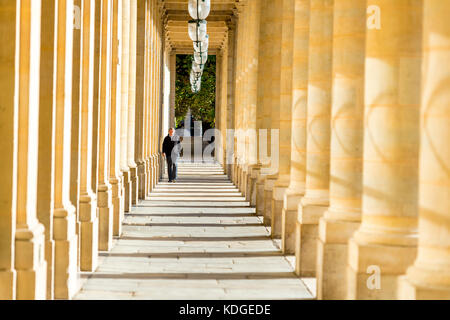 Un homme traverse les arcades couvertes au Palais Royal de Paris, France Banque D'Images