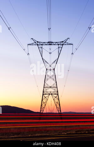 Une longue exposition de pylônes à côté de l'autoroute au coucher du soleil avec des voitures qui passent. Banque D'Images