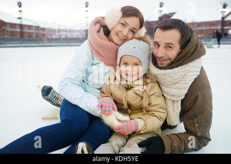 Affectueux et actif dans la famille winterwear assis sur patinoire Banque D'Images